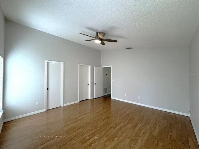 a view of empty room with wooden floor and fan