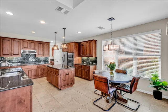 a kitchen with stainless steel appliances kitchen island granite countertop a table chairs and a refrigerator