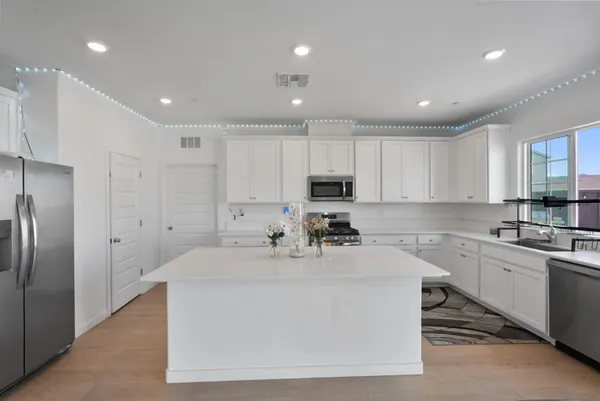 a large white kitchen with kitchen island a sink stainless steel appliances and cabinets