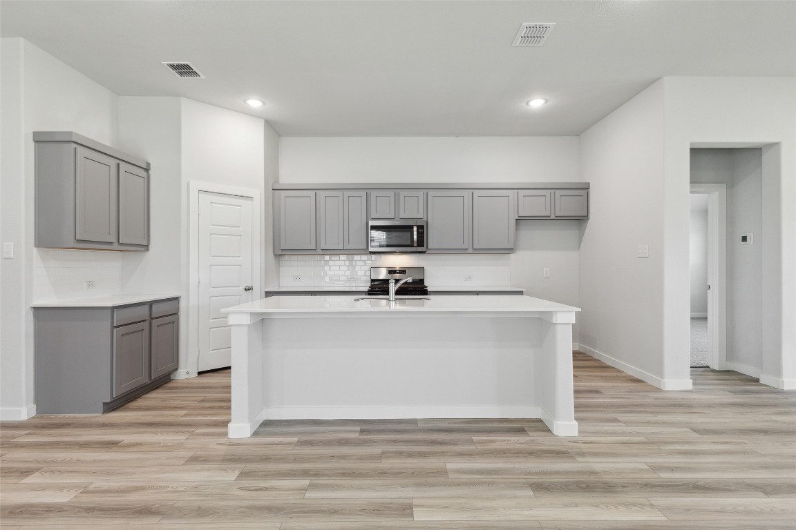 200 Hidalgo Lane Elgin, TX 78621 - Photo 4 of 25 Kitchen featuring gray cabinetry, appliances with stainless steel finishes, a center island with sink, and recessed lighting