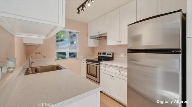 a kitchen with granite countertop a refrigerator a sink and white cabinets