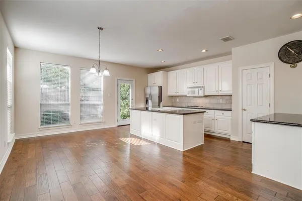 a kitchen with stainless steel appliances granite countertop wooden floors white cabinets and window