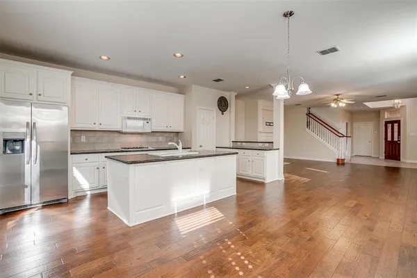 a large kitchen with kitchen island a stove a sink dishwasher a refrigerator and white cabinets with wooden floor