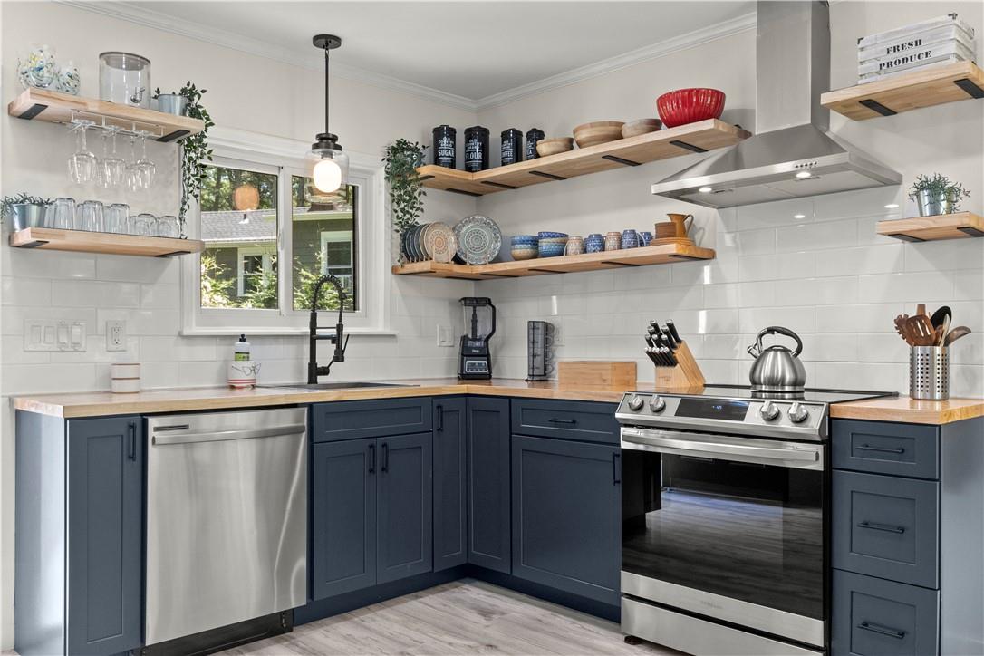 Kitchen featuring exhaust hood, decorative light fixtures, backsplash, sink, and appliances with stainless steel finishes