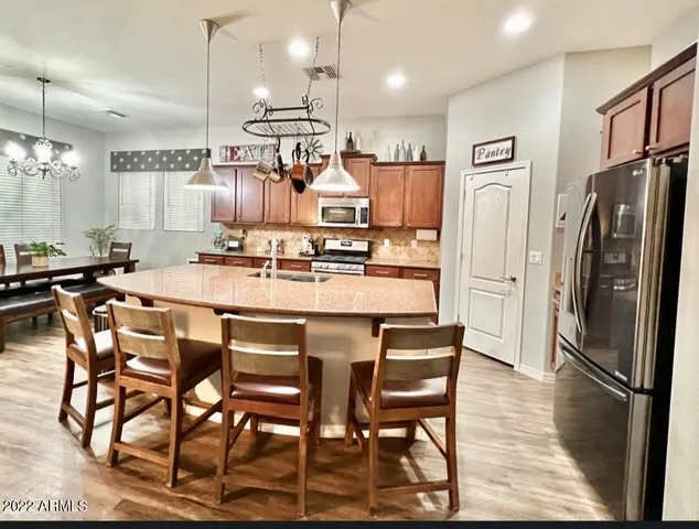 a kitchen with stainless steel appliances kitchen island granite countertop a dining table chairs and a refrigerator