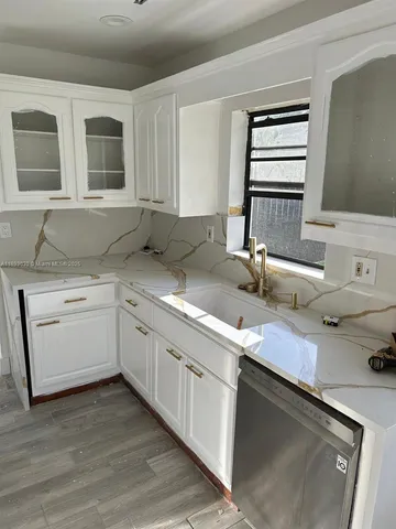 a kitchen with a sink dishwasher and white cabinets with wooden floor