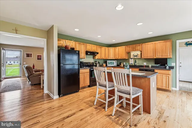 a kitchen with stainless steel appliances granite countertop a sink a stove top oven a refrigerator with wooden cabinets and floor