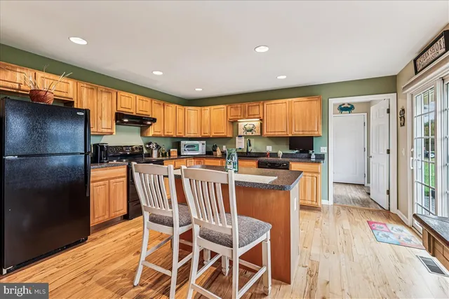 a kitchen with stainless steel appliances granite countertop a stove top oven a sink dishwasher and a refrigerator with wooden floor