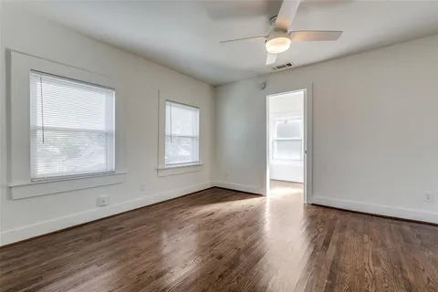 an empty room with wooden floor chandelier fan and windows