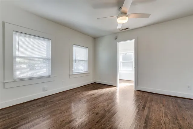 an empty room with wooden floor chandelier fan and windows