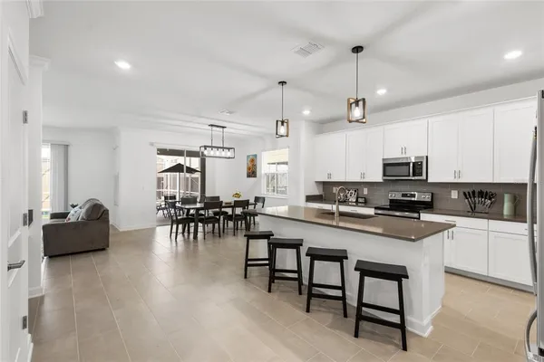 a kitchen with stainless steel appliances granite countertop a stove top oven a sink a dining table and chairs with white cabinets