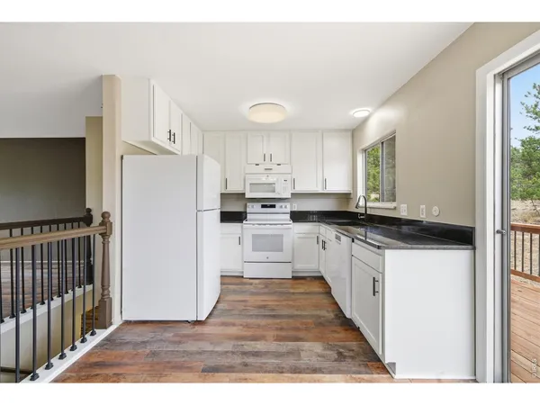 a kitchen with granite countertop a refrigerator oven a sink dishwasher and white cabinets with wooden floor