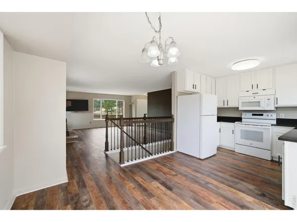 a open kitchen with stainless steel appliances granite countertop a refrigerator a stove a microwave oven a dining table and chairs with wooden floor