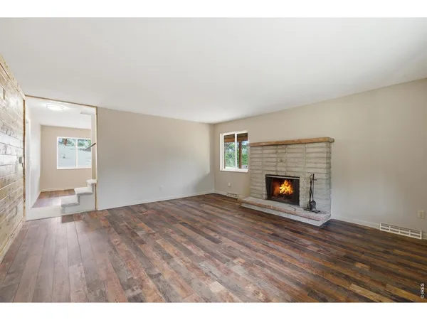 a view of an empty room with wooden floor fireplace and a window