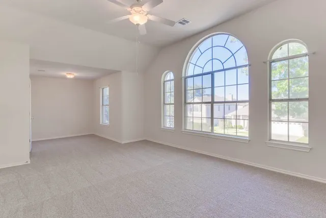 an empty room with windows and chandelier fan