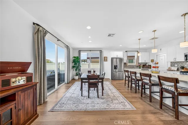 a kitchen with stainless steel appliances kitchen island granite countertop a refrigerator a stove a dining table and chairs with wooden floor