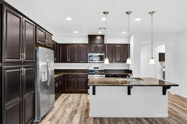 a kitchen with stainless steel appliances granite countertop a refrigerator a stove a oven and a sink with wooden floor