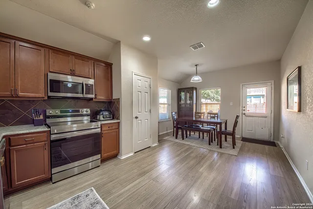 a kitchen with stainless steel appliances granite countertop a stove top oven a sink dishwasher a dining table and chairs with wooden floor