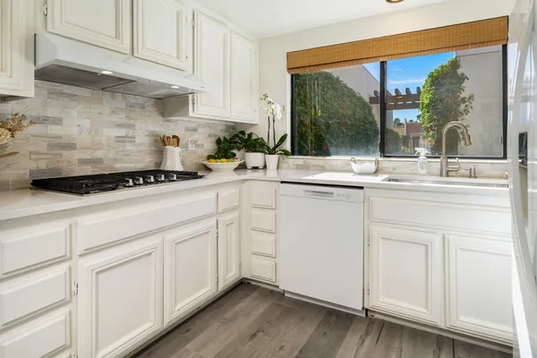 a kitchen with white cabinets a sink and dishwasher with wooden floor