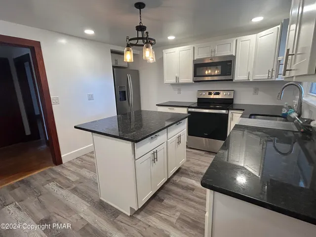 a kitchen with stainless steel appliances granite countertop a sink a stove a microwave a refrigerator a stove and white cabinets