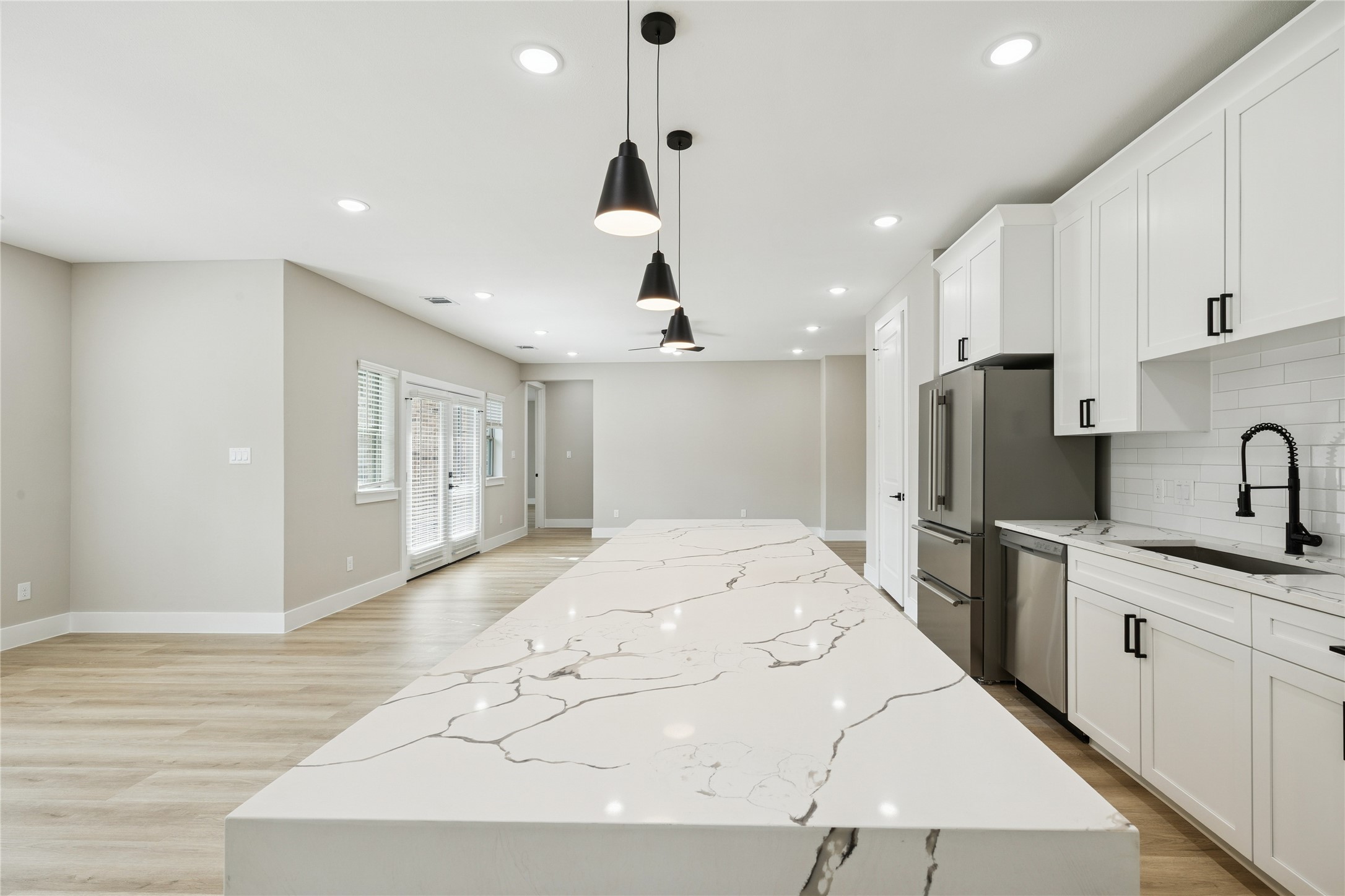 2610 Martinas Court Spring, TX 77388 - Photo 3 of 35 This modern kitchen features a spacious open layout with a large, elegant marble-patterned island, sleek white cabinetry, stainless steel appliances, and stylish pendant lighting. Bright and airy with natural light from large windows.