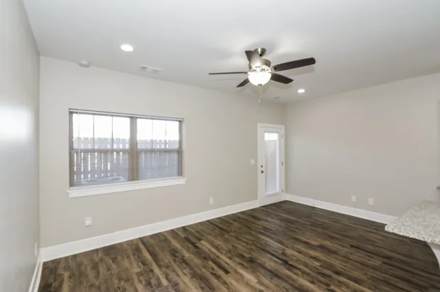 an empty room with wooden floor fan and windows