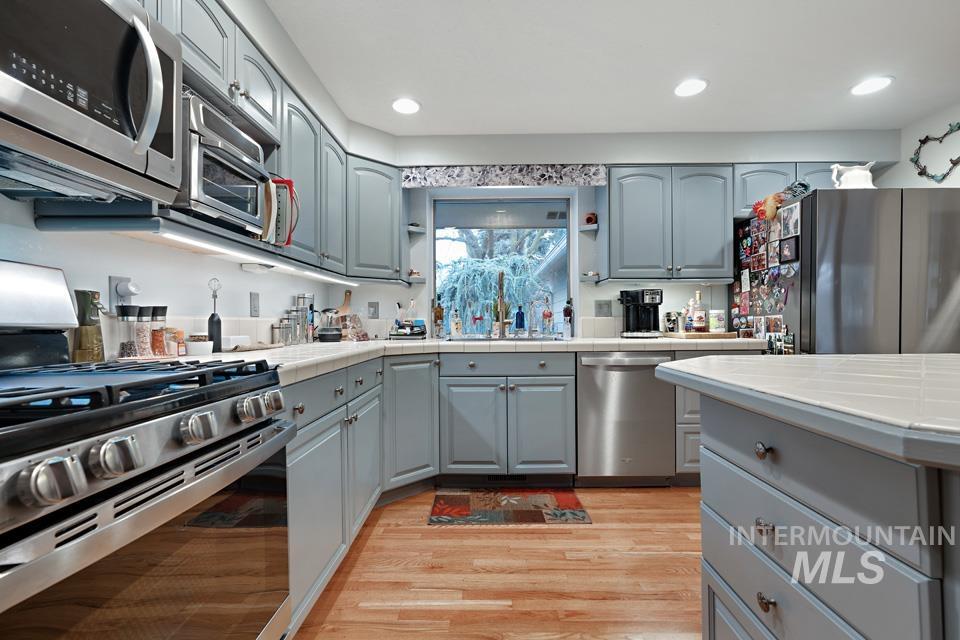9518 Scorpio Street Boise, ID 83709 - Photo 7 of 46 Kitchen with tile counters, stainless steel appliances, light wood-type flooring, gray cabinetry, and recessed lighting