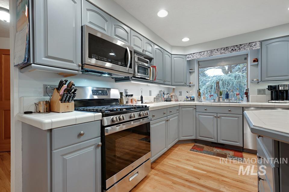 9518 Scorpio Street Boise, ID 83709 - Photo 8 of 46 Kitchen featuring gray cabinetry, tile counters, appliances with stainless steel finishes, light wood-type flooring, and recessed lighting