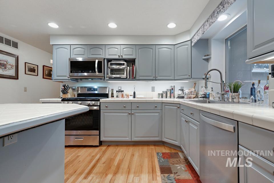 9518 Scorpio Street Boise, ID 83709 - Photo 9 of 46 Kitchen with tile counters, gray cabinetry, appliances with stainless steel finishes, light wood-style flooring, and recessed lighting