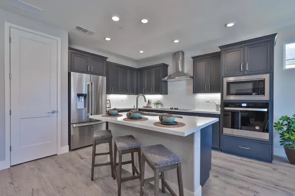 a kitchen with stainless steel appliances granite countertop a refrigerator a stove a sink and a oven with wooden floor