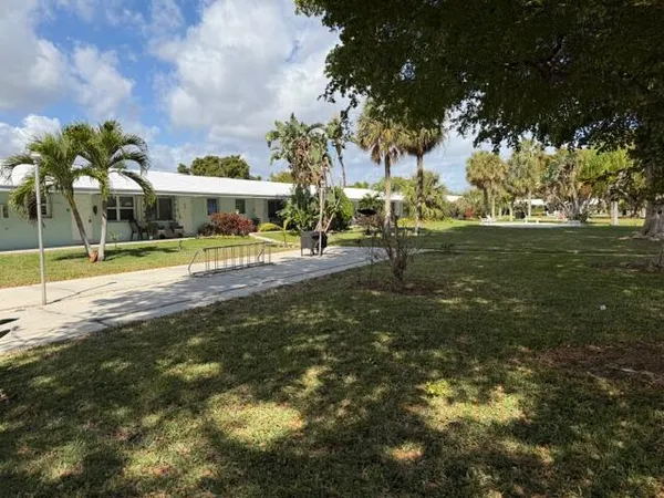 a view of a house with a big yard and palm trees