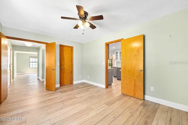 a view of an empty room with wooden floor and a ceiling fan