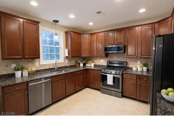 a kitchen with stainless steel appliances granite countertop wooden cabinets a sink a stove a refrigerator and island with wooden floors