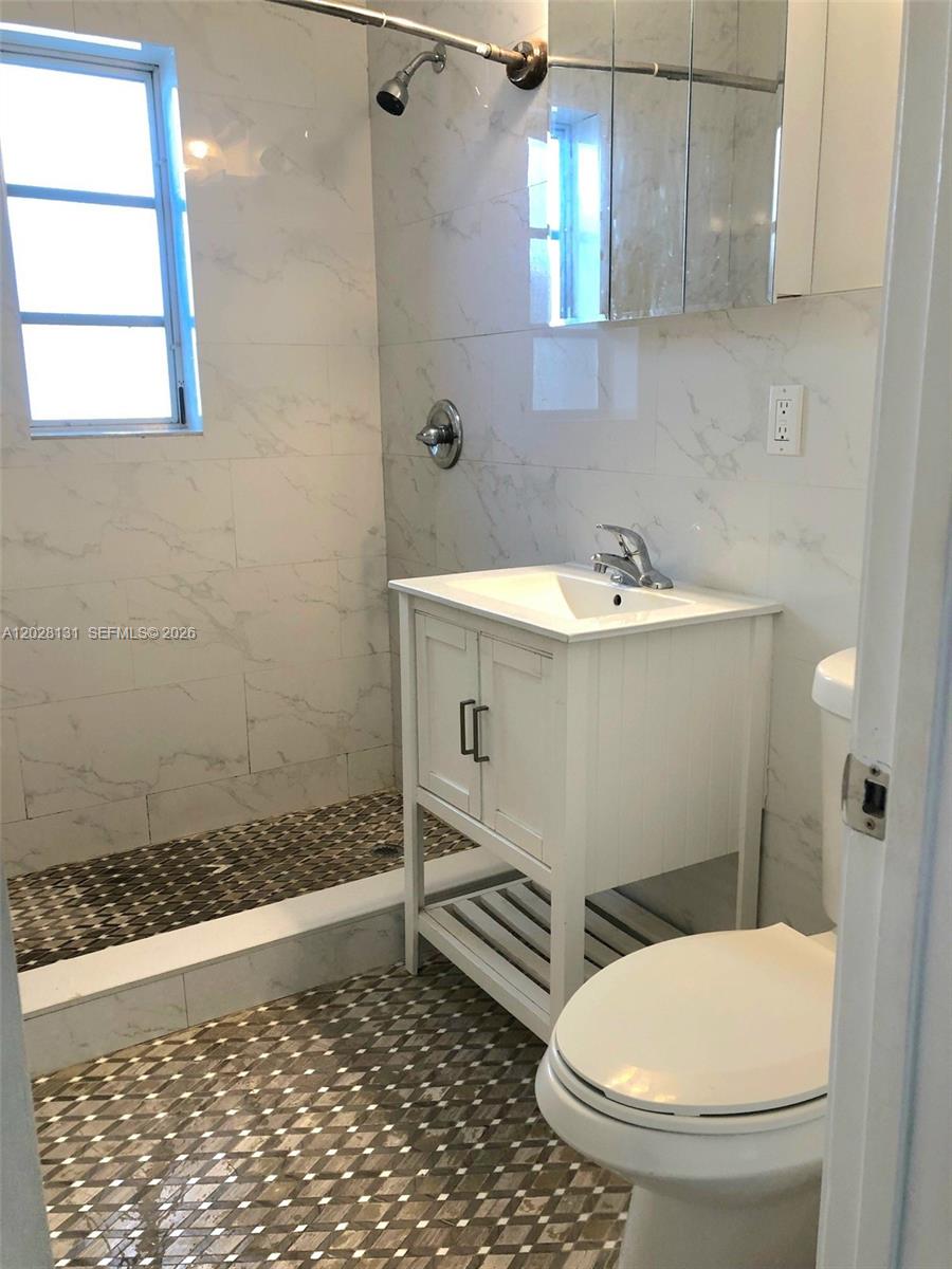 7135 Rue Granville, Unit 4 Miami Beach, FL 33141 - Photo 4 of 9 a bathroom with a sink a toilet a window and vanity