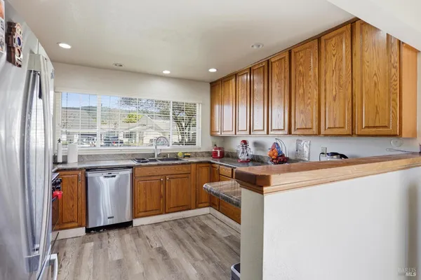 a kitchen with stainless steel appliances granite countertop a stove a sink dishwasher and a refrigerator with wooden floor