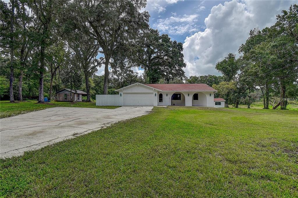 6234 Neff Lake Road Brooksville, FL 34601 - Photo 4 of 59 a view of a white house in front of a big yard with plants and large trees