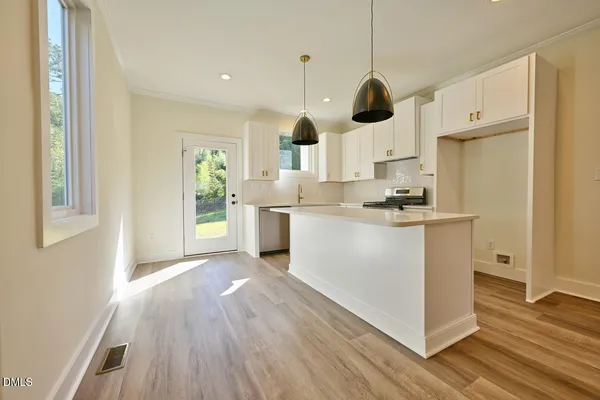 a kitchen with kitchen island stainless steel appliances a stove a refrigerator a sink a dining table and wooden floors