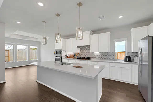 a kitchen with stainless steel appliances granite countertop a sink a stove a refrigerator and island with wooden floor