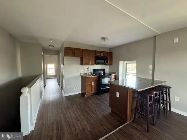 a kitchen with granite countertop a refrigerator a stove a sink a dining table and chairs with wooden floor