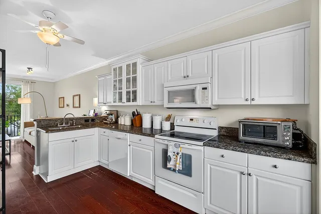 a kitchen with stainless steel appliances granite countertop white cabinets a sink a stove a dining table and chairs