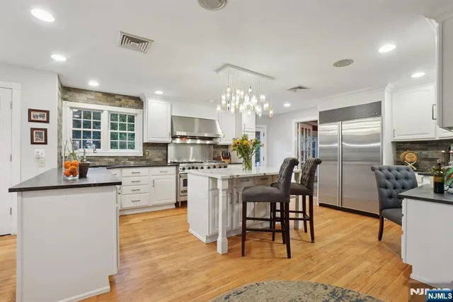a kitchen with stainless steel appliances kitchen island granite countertop a table chairs and a refrigerator