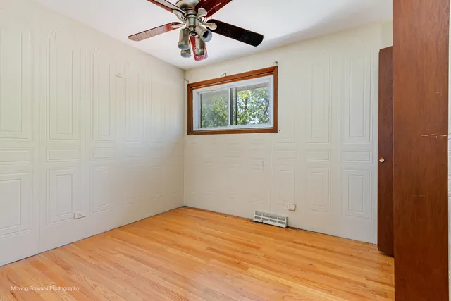 an empty room with wooden floor ceiling fan and windows