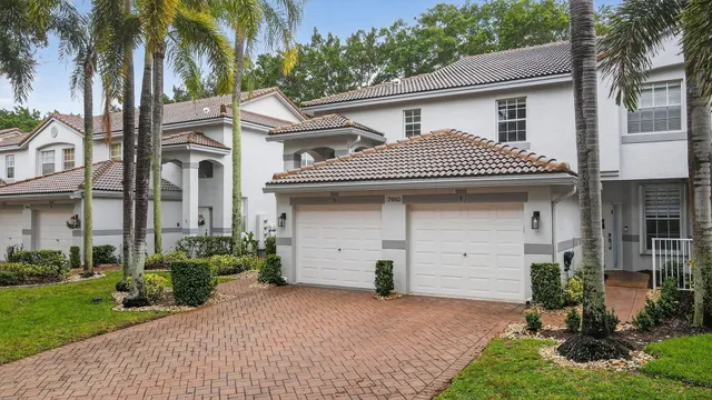 a view of a white house with a large windows and a yard with plants and palm trees