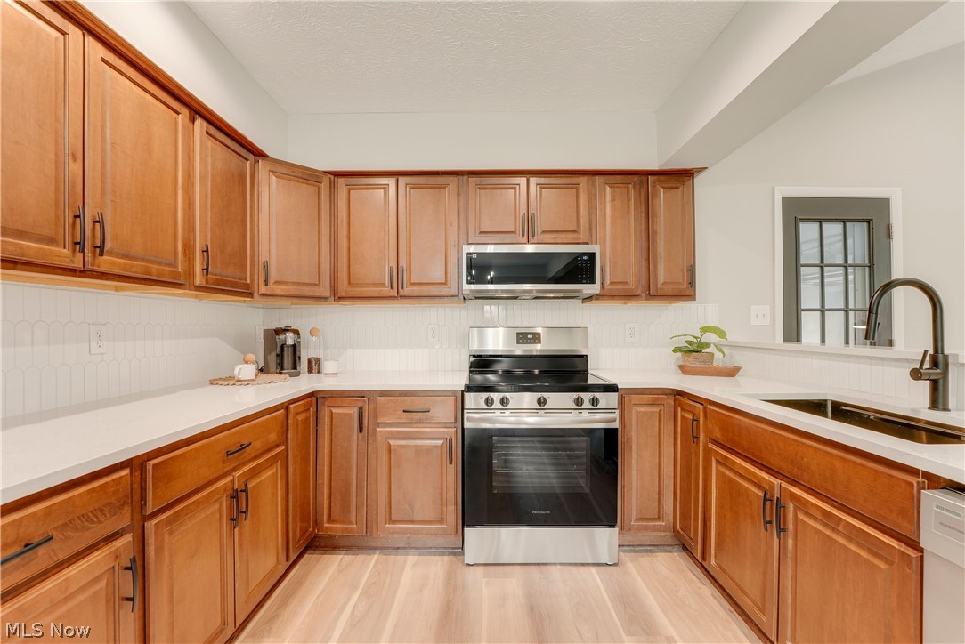 646 Ledge Road Macedonia, OH 44056 - Photo 7 of 28 U-shaped kitchen featuring wood cabinetry, light countertops, white tile backsplash, a stainless steel range, and a stainless steel microwave