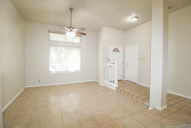 an empty room with chandelier fan and windows