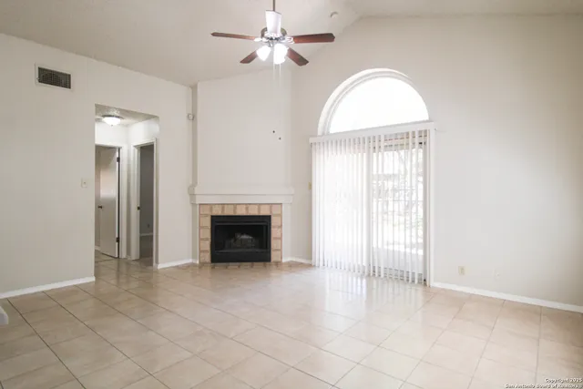 an empty room with windows chandelier fan and fireplace