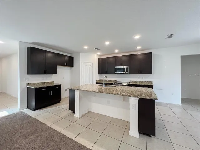 a kitchen with stainless steel appliances kitchen island granite countertop a stove top oven a sink a microwave and a refrigerator