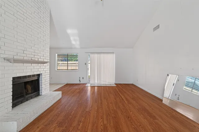a view of an empty room with wooden floor fireplace and a window