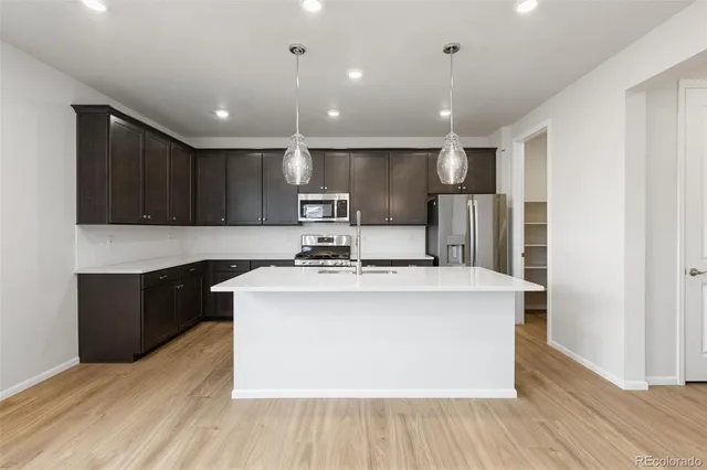 a kitchen with kitchen island stainless steel appliances a sink a stove a refrigerator cabinets and wooden floor