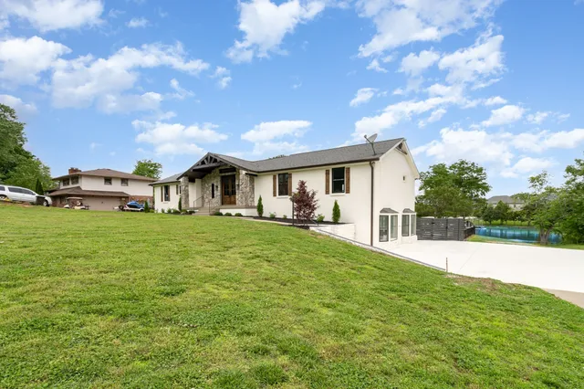 a view of a white house in front of a big yard with plants and large trees
